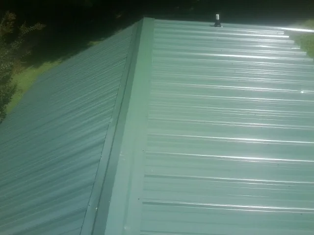 New green metal panels meeting at the ridge of a roof — Flat Roof Repair work by our crew in Franklinville