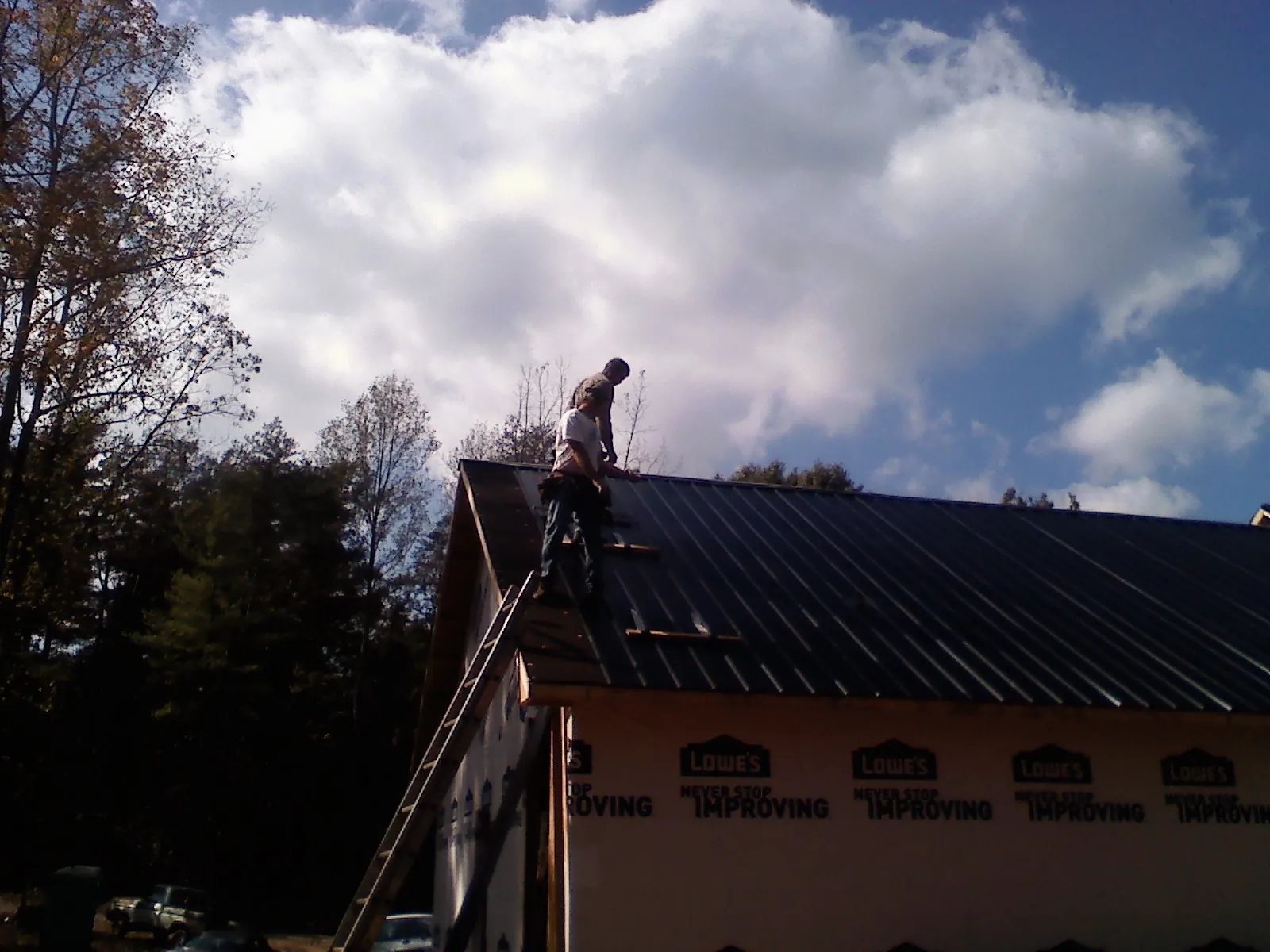Roofer fastening dark metal panels high against a cloudy sky, from a Roof Inspection job in Franklinville
